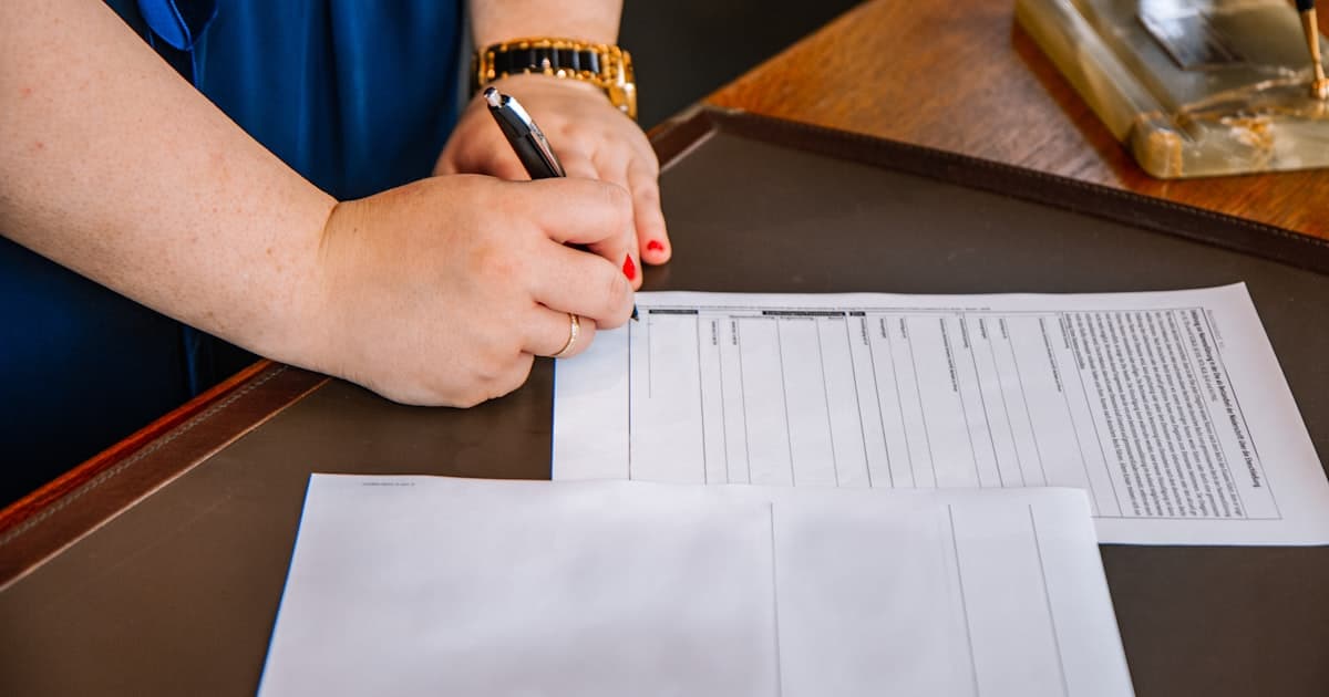 Main signant un document administratif officiel sur un bureau, illustrant le dépôt d'un dossier de renouvellement de carte professionnelle