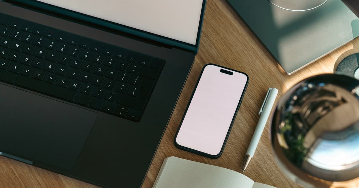 Bureau avec ordinateur portable, telephone et carnet de notes, illustrant les outils numeriques utilises par les agents immobiliers