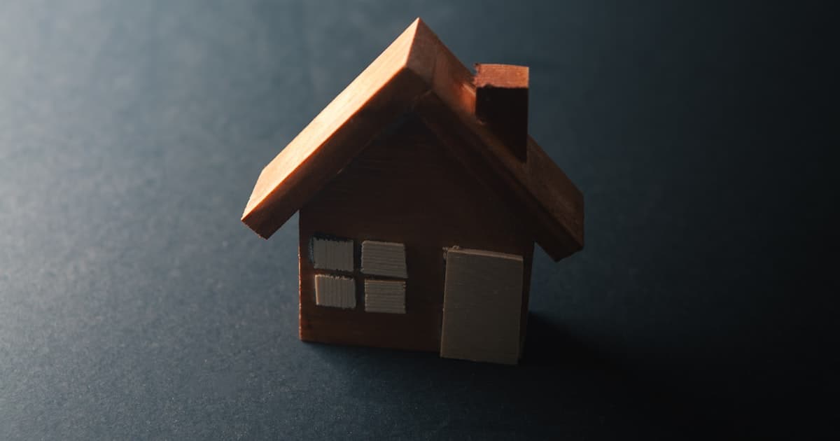 Maquette de maison en bois eclairee dans la penombre, illustrant le bien confie par mandat de vente a un professionnel de l'immobilier