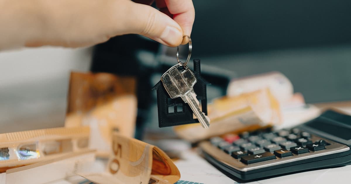 Main tenant une cle de maison devant une calculatrice et des billets en euros, illustrant le calcul d'une capacite d'emprunt