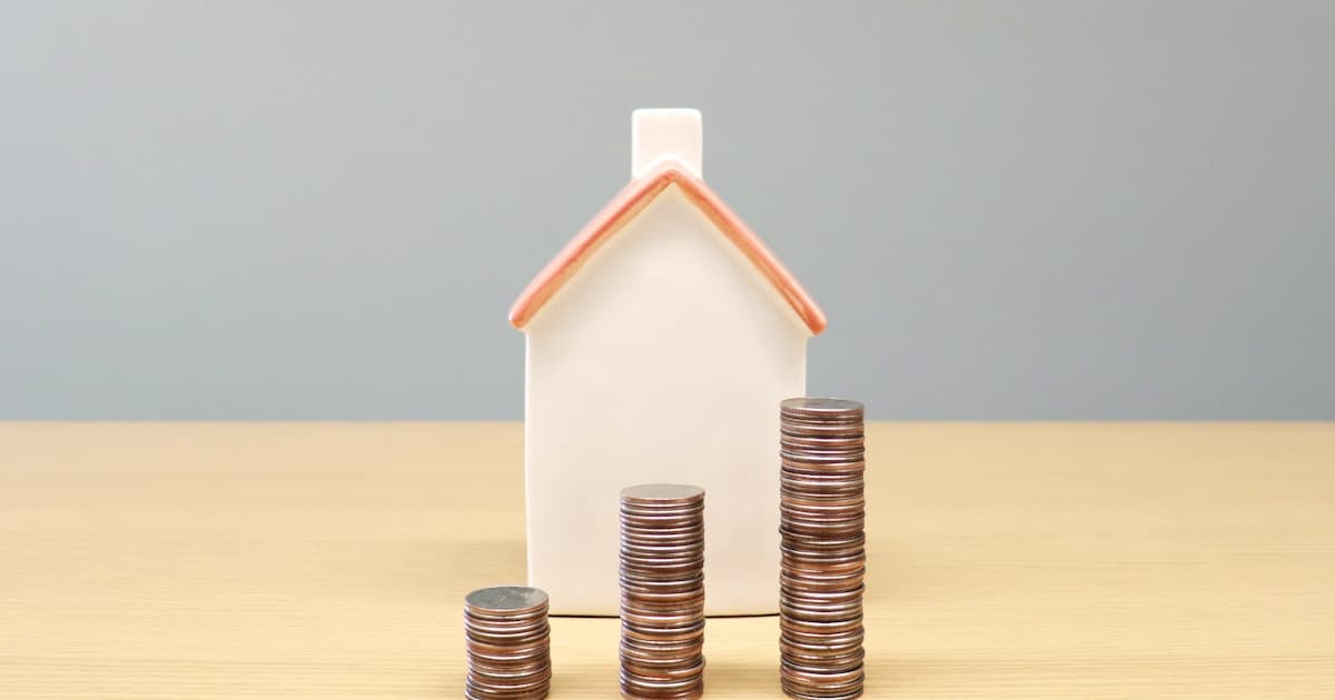 Petite maison en ceramique entouree de piles de pieces de monnaie croissantes, illustrant les garanties de pret cautionnement et hypotheque